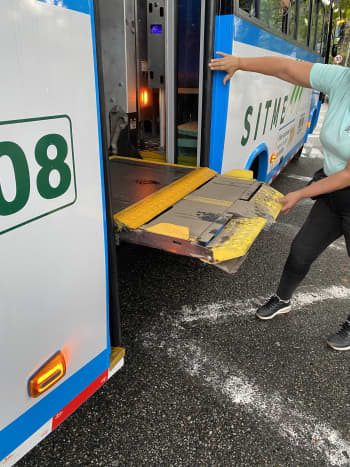 Un bus azul con blanco del SITME con la plataforma de sillas de ruedas extendida mientras un usuario intenta destrabarla para que opere correctamente.